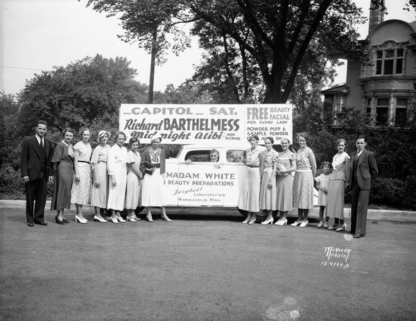 Group portrait of "Madame White" cosmetics sales staff with car and signage for an event at the Capitol Theatre with Richard Barthelmess in "Midnight Alibi." Signage advertises Madame White Beauty Preparations, Bergholt Laboratories, Minneapolis, Minnesota.