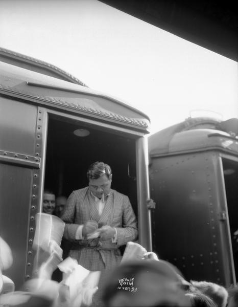 Babe Ruth, wearing a dressing gown, standing in the doorway of a train car and signing autographs.