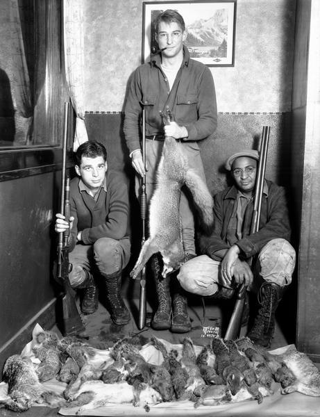 Three hunters posing with shotguns and their bounty of a fox, squirrels and rabbits. The man on the right may be UW-Madison chef Carson Gulley.