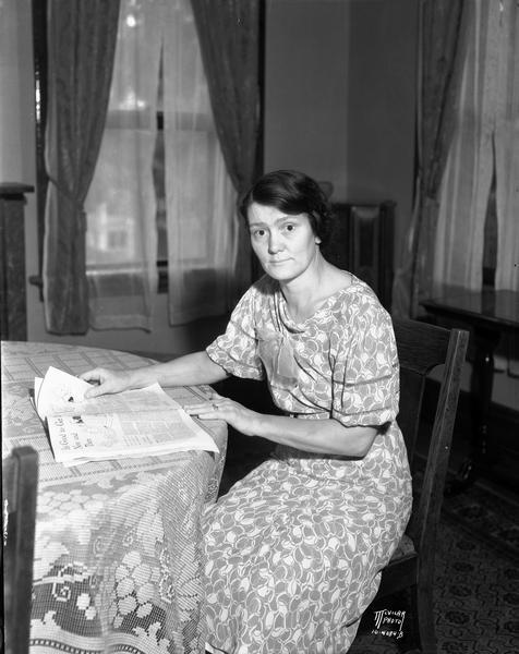 Portrait of Martha Finn, jail matron and wife of Sheriff Fred T. Finn, sitting at a table, reading a newspaper. Her duties consist of cooking for all the jail inmates as well as caring for women prisoners and ill prisoners. She also cares for her family of four children.