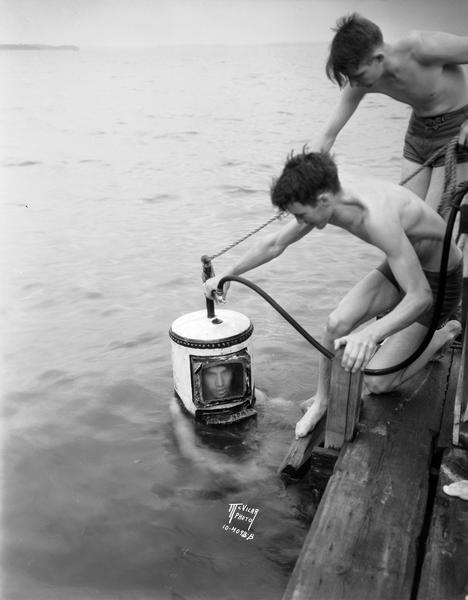 Edgar Tullis, in the water wearing a diving helmet, is assisted by Jerry Randall and Lyell Tullis, standing on a pier.