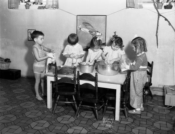 Five children are washing dishes at the Dorothy Roberts nursery school at the University of Wisconsin Home Economics practice cottage.