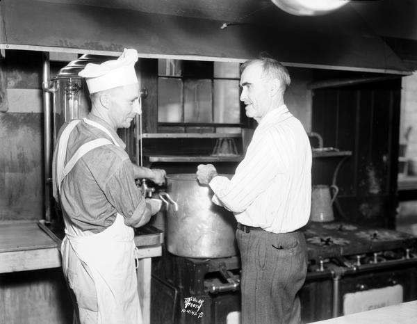 Director Tom C. Gannon, (on the right) and Assistant Chef Ed Masury in apron, who is drawing a cup of coffee, standing at the stove in the transient home kitchen, 9 South Webster Street.