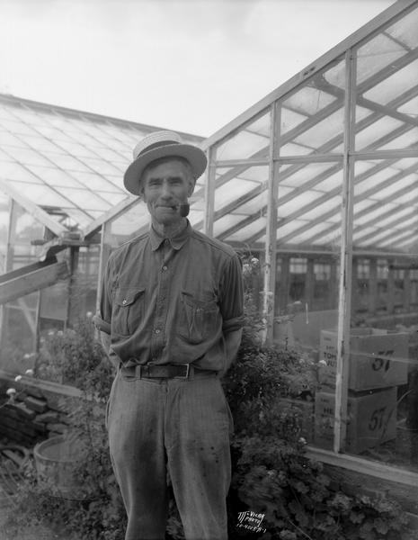 John Walker, father of 16 children, standing outside a greenhouse with a pipe in his mouth.