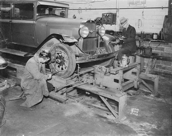 Two men inspecting an automobile on the RITE-Way wheel aligning and axle-straightening machine at Schultz Tire and Battery Co., 1336 Regent Street.