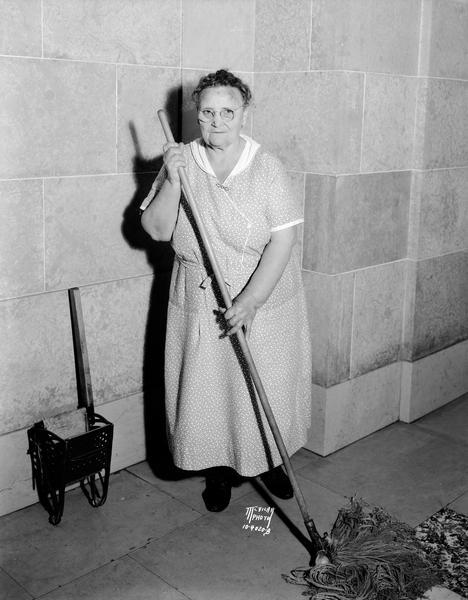 Mrs. Mary DeRenzo, "Dean of the scrub women's crew" at the Wisconsin State Capitol, holding the mop she used for thirty years.