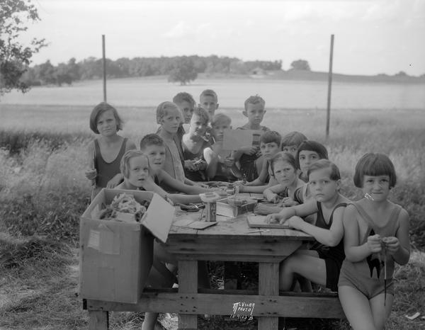 A group of children around a picnic table posing while doing crafts at The Capital Times Kiddie Camp.