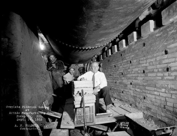 A.H. Hubbell Company workers build a "Complete Plibrico Jointless Firebrick Lining" brick wall around a boiler in the engine room at Arcade Manufacturing Co.