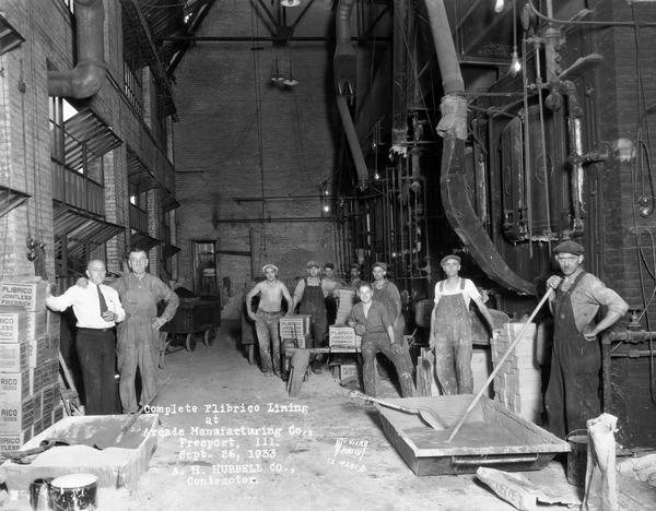 Nine brick layers with supervisor in engine room. Caption on print reads: "Complete Plibrico Jointless Firebrick Lining at Arcade Manufacturing Co., Freeport, ILL., A.H. Hubbell Co., contractor."