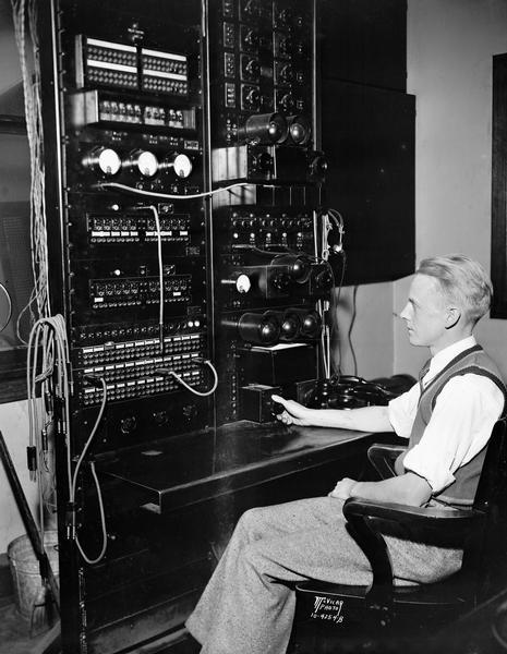 A man is sitting at a master control in the WIBA radio control room, 111 King Street.