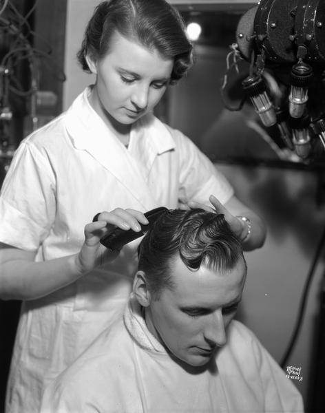 Cedric Parker, Capital Times newsman, has Lucille Bump, beauty operator give him a Rudy Vallee fingerwave at Mrs. Wengel's Marinello Shop, 125 State Street.
