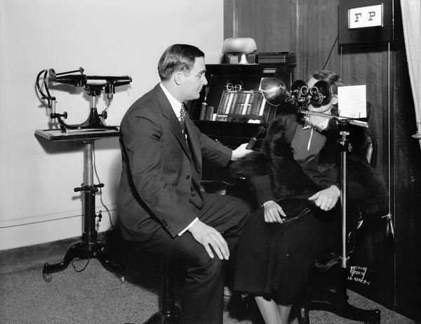 Dr. John E. Hughes, optometrist, tests a patient's vision in his office at 112 E. Main Street, using an eyeglass lens machine.
