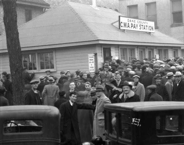 Men crowd around the newly opened Dane County C.W.A. Pay Station at the corner of West Dayton and North Carroll Streets to pick up paychecks.