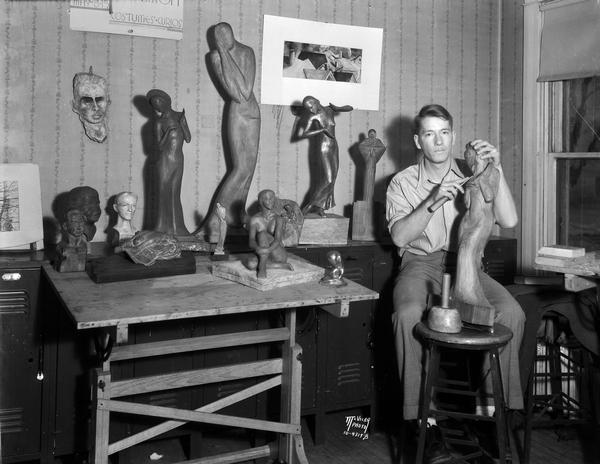 University of Wisconsin student sculpting a statue. He is surrounded by small sculptures in the old student Union building.