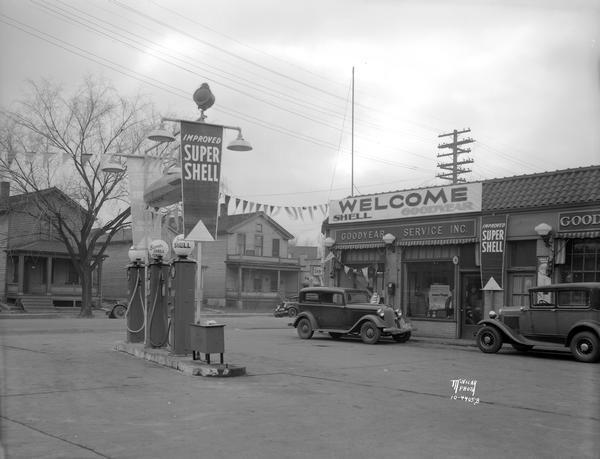 Goodyear Service Station and Shell Gas, 205 N. Bassett Street at W. Dayton Street with Super Shell gas pumps and two automobiles parked in front. Houses across the street are at 208 and 212 N. Bassett Street.