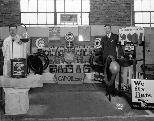 Two men stand with the Capitol Oil Corporation display at the Madison Auto Show.  The exhibit features "Tiolene Motor Oil," "Bowes Seal Fast," "Purol-Pep gasoline," "General Batteries," and "Yale Tires."