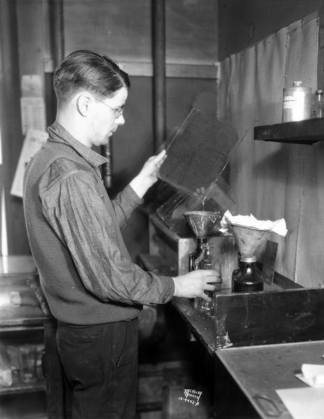 A man in the camera room at the Wisconsin Engraving Company plant, 109 S. Carroll Street, is coating the wet plate negative with rubber and collodion to make the film durable enough for its removal from the negative glass, the second step in making a photo engraving plate.