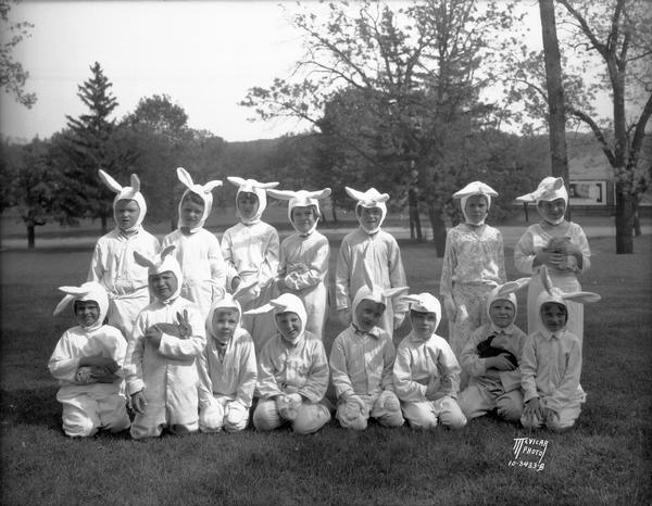 Group portrait of children, some of them holding rabbits, wearing rabbit costumes posing on the grounds of Dudgeon School, 3200 Monroe Street. Mrs. Hayes.