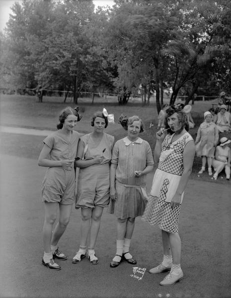 Blackhawk Country Club "Childrens Day," women's dress up golf event. Four women are wearing children's dresses and eating lollipops.