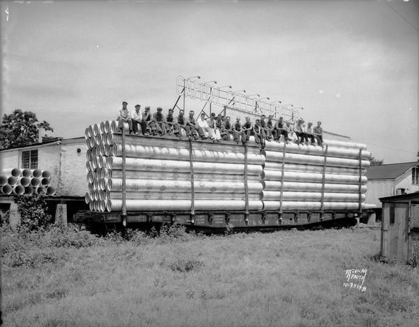 Group of men sitting on top of railroad flatbed car loaded with culverts. Sign above them reads: "Capital City Culvert Company," 1335 Gilson Street.