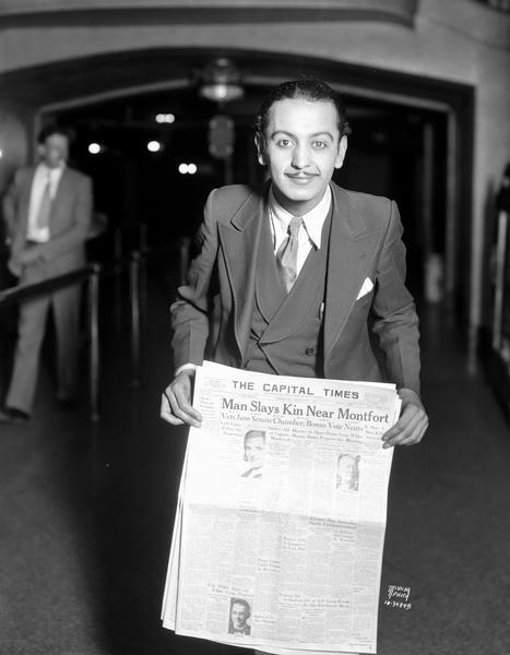 Pablo the Magician holding a "Capital Times" newspaper in the lobby of the Orpheum Theatre. He is using the newspaper in his act with Fanchon and Marco's show, "Gobs of Joy in Bermuda."