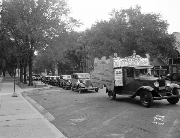 A "RKO Greater Show Season" truck with signs promoting a show at the RKO Orpheum Theatre, a calliope and two men sitting on top, leading a parade of automobiles on Wisconsin Avenue.