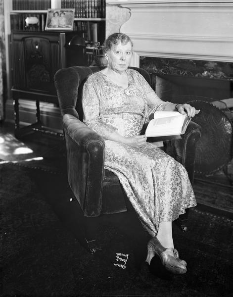 Portrait of Kate Schmedeman, Mayor Albert G. Schmedeman's wife, sitting in a chair beside a fireplace reading a book in her home, 504 Wisconsin Avenue.