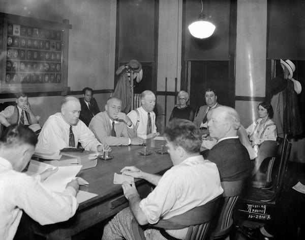 Trial of Madison Police Dept. Desk Sargent Jesse M. Smith, accused of non-payment of a $191 bill which his ex-wife incurred at the Dean clinic. This was held before the Board of Police and Fire commissioners. In the lower left, his back to the camera, is City Attorney Theodore G. Lewis who acted as prosecuting attorney. Seated at the table, and to the left of Mr. Lewis are Police Chief William H. McCormick, Dr. William F. Lorenz, and Sec. Joseph H. Brown. The woman in the background, near Brown, is Mary Grane, clerk of circuit court. Next in order is George F. O'Connell, commission president. Marjorie Johnson is in the upper right. To her left, only partially visible, is the shorthand reporter. Next is Commissioner George Sayle. The man in the immediate foreground is a newspaper reporter.