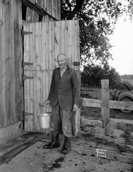 Farmer Charles Nelson, carries a pail in front of the door to his barn. His 245 acre farm was southwest of Lake Wingra near Madison. It became the first property bought for the U.W. Arboretum.