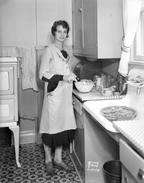 U.W. co-ed, Maybelle Goodyear of Sauk City, earns money to pay for school by preparing a meal in the kitchen of Dr. and Mrs. C.R. Mooney, at 306 Virginia Terrace.