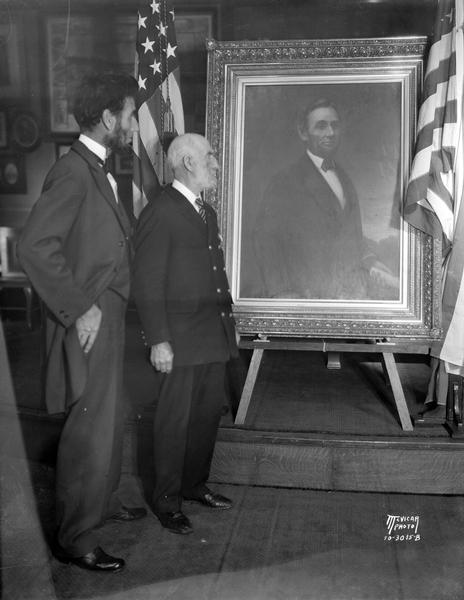 Abraham Lincoln impersonator, Charles E. Bull, of Hollywood, California, and Jesse S. Meyers, commander of the Madison G.A.R. post, stand in front of a portrait of Lincoln in the G.A.R. room in the Wisconsin State Capitol.