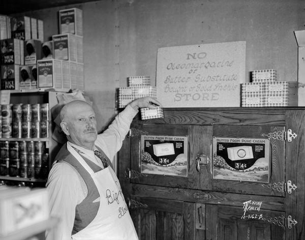 Clinton Bullard holding a package of butter next to a sign that reads: "No Oleomargarine or Butter Substitutes Bought or Sold in this Store," in his store at 5372 Old Middleton Road, at Glen Oak Hills.