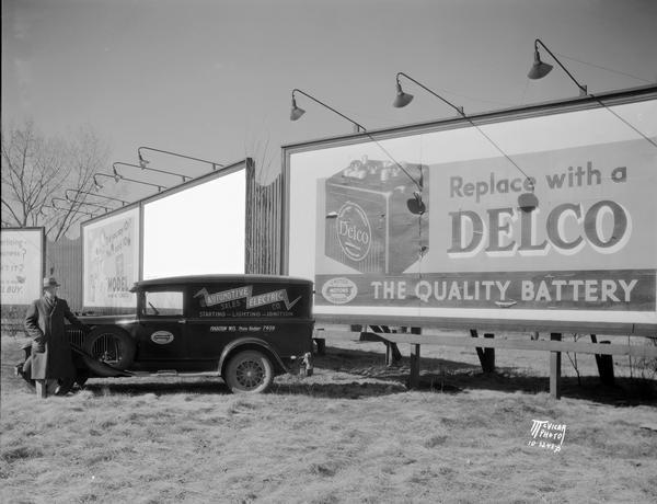 A man stands with an Automotive Electric Company truck in front of a Delco Battery billboard.