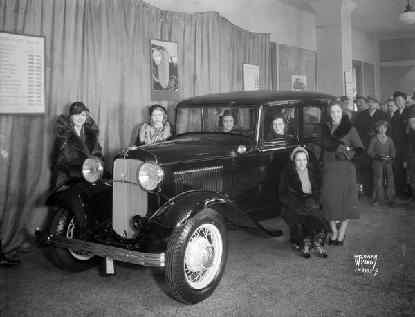 Six Lido Ladies, an act performing at the Orpheum Theatre, posing with a new Ford V8 car in the lobby of the Orpheum Theatre with a crowd looking on.
