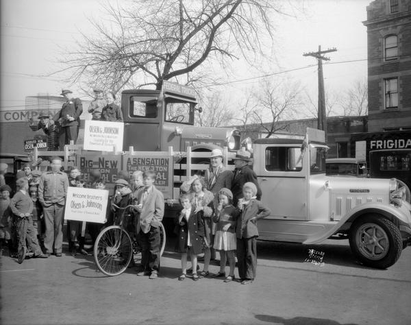 Surrounded by onlookers, Ole Olsen and Chic Johnson are riding in a wire cage on the back of a "Federal" brand truck. The truck is on the bed of another "Federal" brand truck and is used to promote their show "Atrocities of 1932" at the Orpheum Theatre.