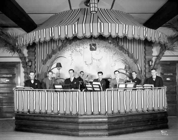 The musicians of the Chanticleer orchestra sitting in the bandstand with their instruments and sheet music.
