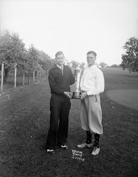 Two golfers hold up a trophy cup at Nakoma Golf Course.