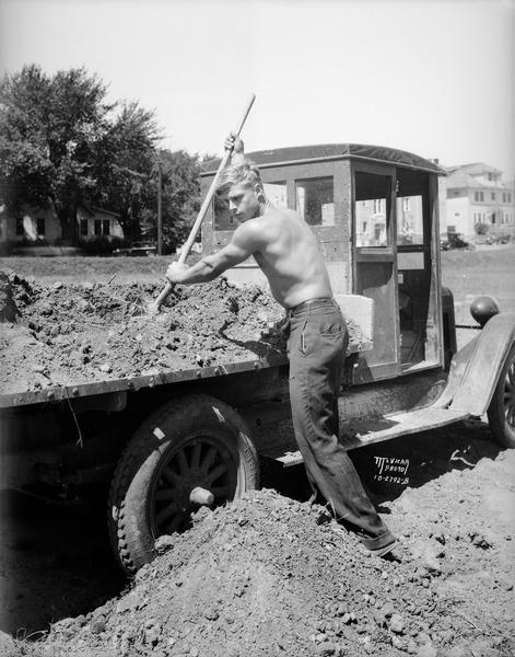Greg Kabat, University of Wisconsin football player, shovels dirt from the back of a truck at Camp Randall.