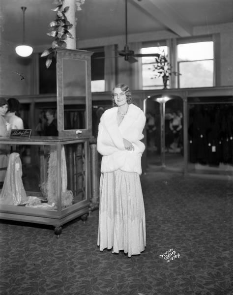 Miss America, Margaret Ekdahl, models a blue and rose Moire evening gown with a short white Dolman fur wrap, at the Burdick & Murray Department Store.