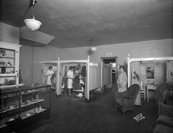 Beauty operators work on customers in booths while another woman waits in the Comf'y Marcel Beauty Shoppe, 2039 Winnebago Street. Moved to 1917 Winnebago Street after 1930.