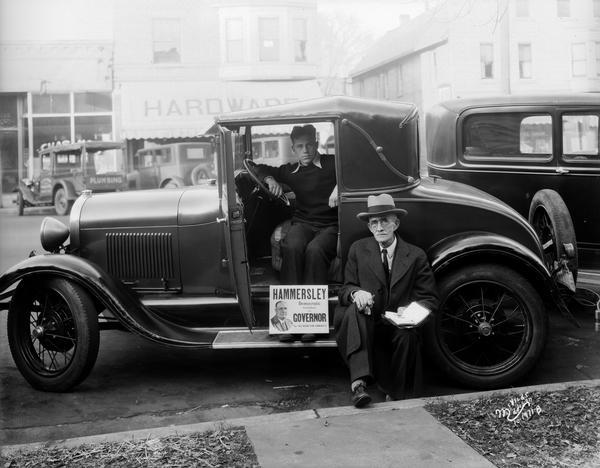 Mr. Cranefield and another man posing with a campaign sign in support of Hammersley for Governor of Wisconsin. One man is sitting in the driver's seat, and the other man is sitting on the running board of the automobile.