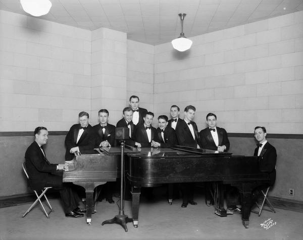 WIBA's "Harvesters" orchestra, wearing tuxedos, gathers for a group portrait  behind two grand pianos at the WIBA studios.
