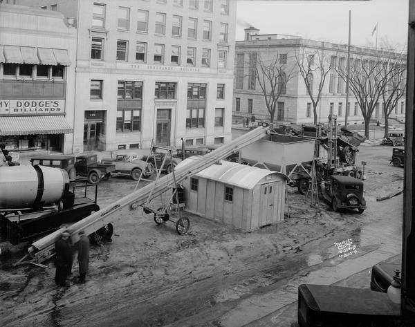 Elevated view of Wisconsin Machine and Foundry road construction equipment, featuring a new portable rock crushing plant, on display at Road Show on Monona Avenue (Martin Luther King Boulevard). Also included in the view are Jimmy Dodge Lunch-Billiards, 117 Monona Avenue, Beaver Insurance Building, 119-123 Monona Avenue, the U.S. Post Office and Federal Court Building at 215 Monona Avenue and a Trachte "office building" for the Wisconsin Machine and Foundry Company.