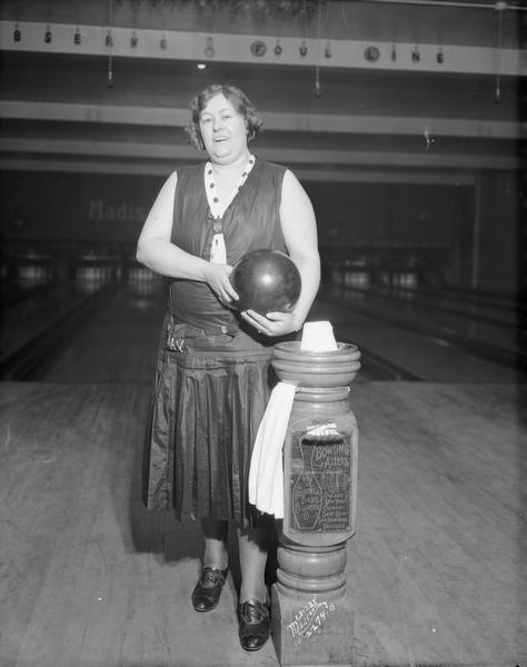 Record setting woman bowler, Nora Kay, Janesville, standing next to Brunswick Balke Collender Co. chalk and towel stand at Madison Bowling and Billiard, 112 N. Fairchild Street. The photograph was taken during the 12th annual Women's State Bowling Meet.