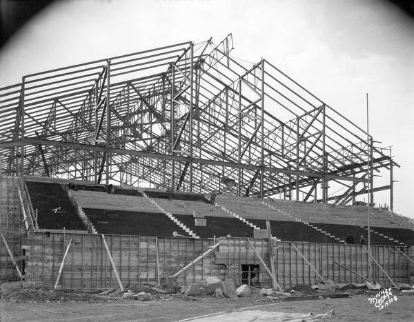 The University of Wisconsin-Madison Field House frame under construction, with novoid corkboard being installed on the south bleachers of Camp Randall in the foreground.