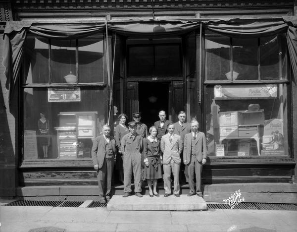 Mitchell Sales Company sales force posing in front of the store, 204 East Main Street. Kitchen ranges are on display in the windows.