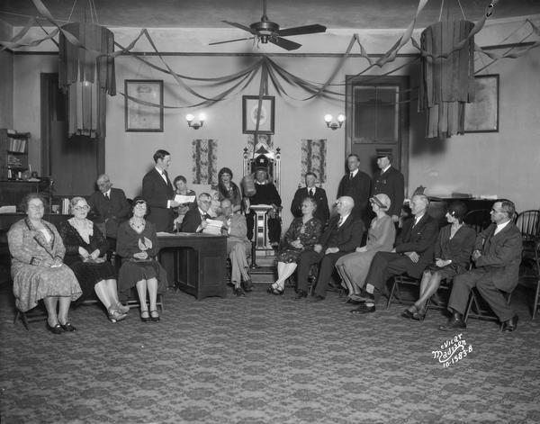 Men and women are seated in a "Mock Trial" as part of the I.O.O.F. 111th anniversary program at the Independent Order of Odd Fellows hall. The hall is decorated for the occasion, at 308 W. Mifflin Street.