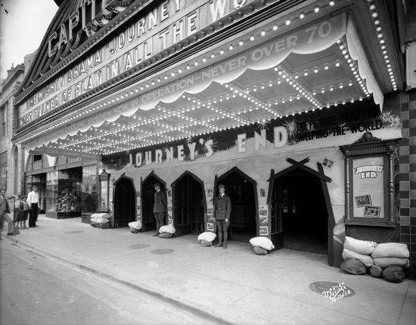 A man and children are standing under the Capitol Theatre marquee that is promoting the movie "Journey's End," with two men dressed as World War I soldier "doughboys" and sandbags around the doors, at 209 State Street.