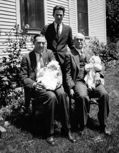 Four generation family group portrait of a great grandfather, a grandfather, the young father, and his twin babies in the laps of the elders.