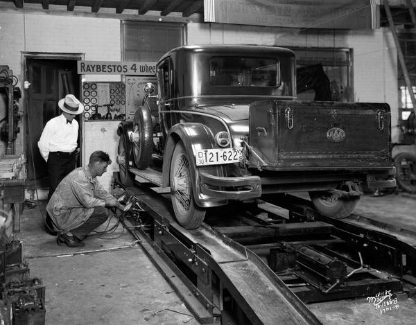 A worker tests the brakes on a car at Schultz Battery, Tire and Supply Company, 1336 Regent Street, while another man watches.